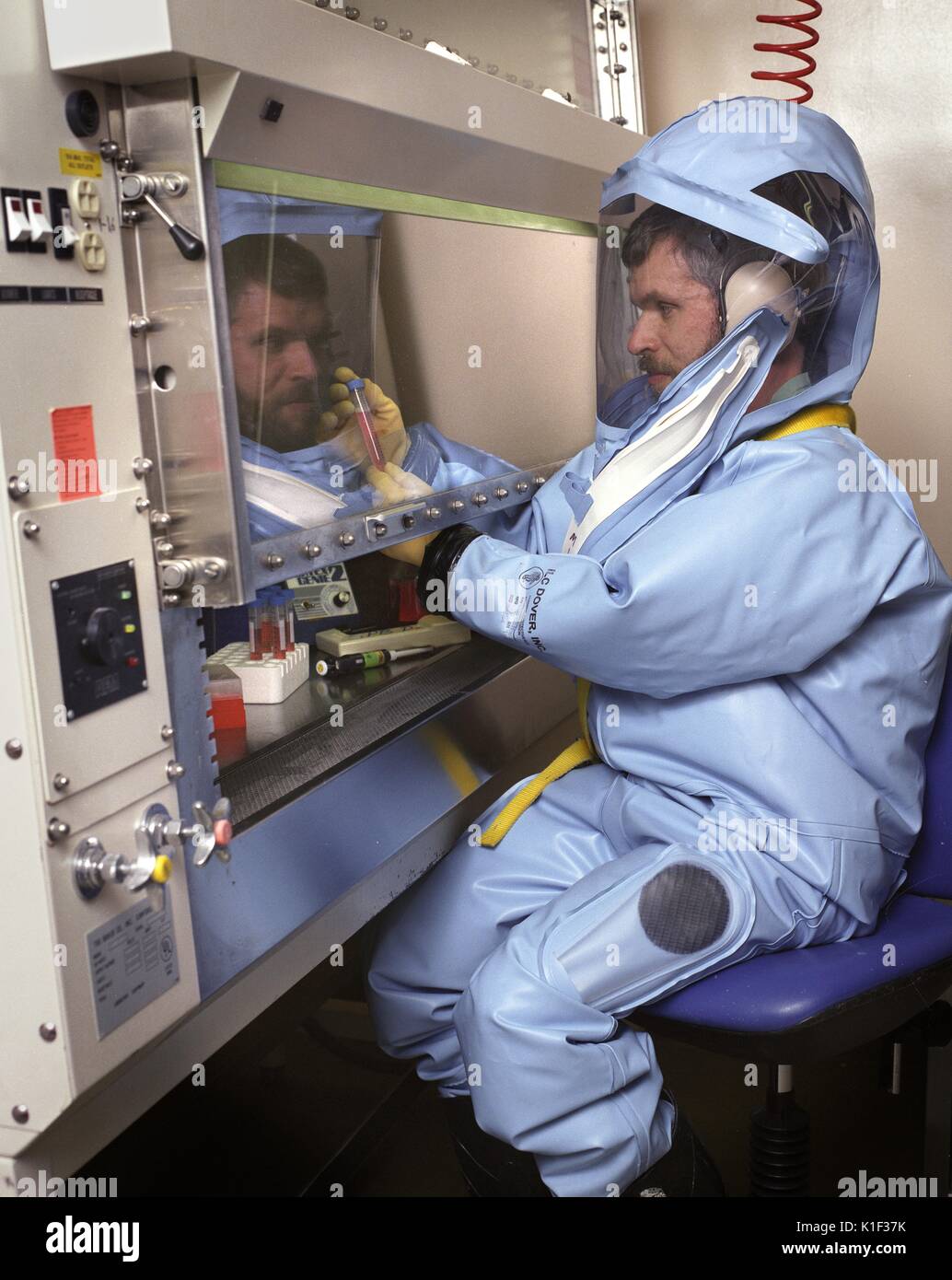 A CDC scientist conducts laboratory research in the Biosafety Level 4 laboratory, Atlanta, GA. LabScience, A CDC scientist wearing a protective suit with helmet and face mask is seated at an air flow hood as he conducts his studies. Image courtesy CDC, 2002. Stock Photo