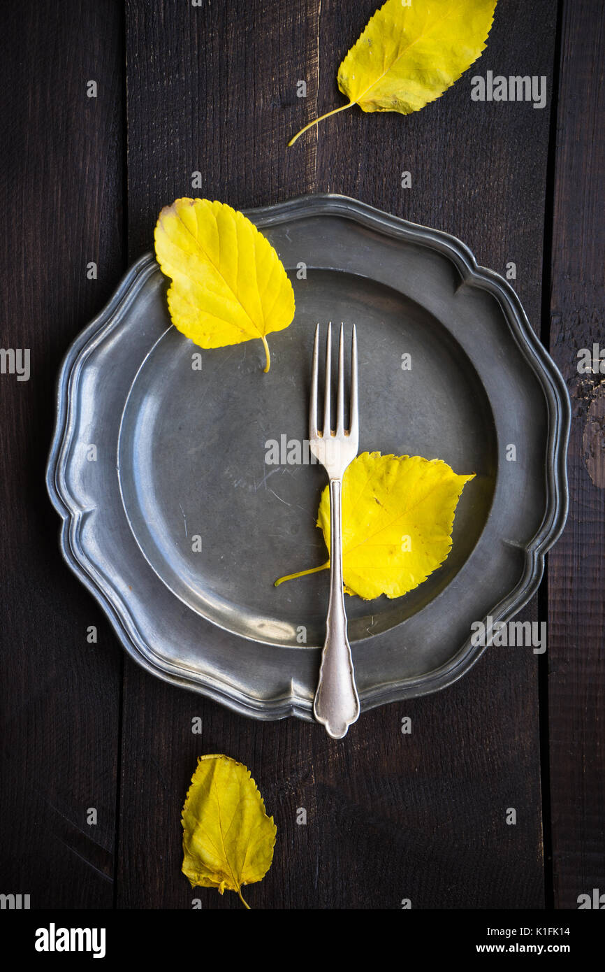 Autumnal table setting with bright yellow leaves and rustic plates on