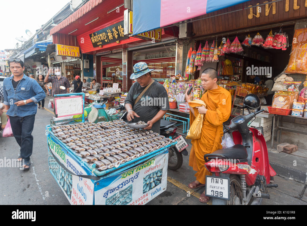 A Thai Buddhist monk purchases fresh fish from a vendor on Maha Chai seafood market, in Thailand. Stock Photo