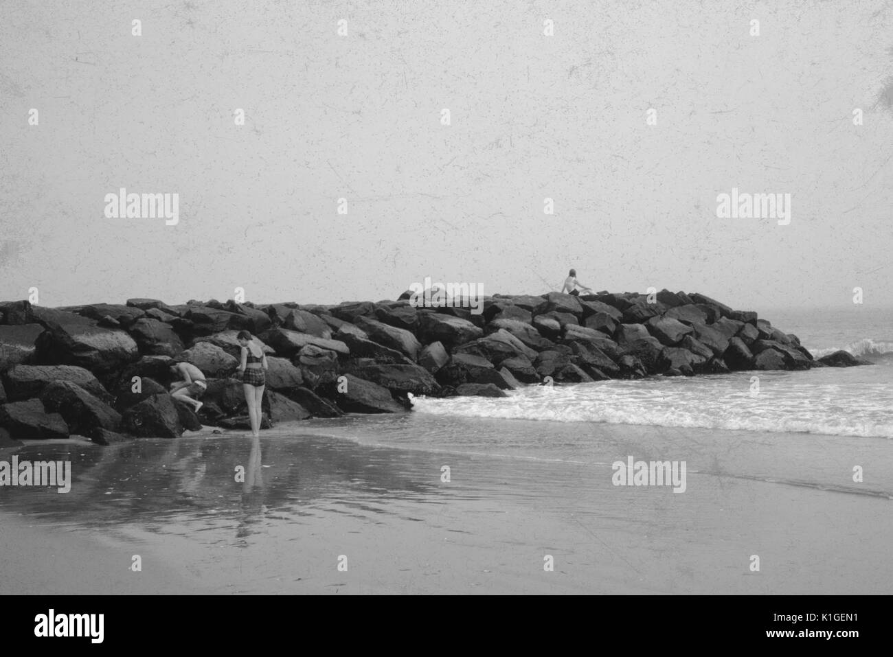 A man and a woman to the side of rocks, a woman on top of the rocks, at a beach, 1966. Stock Photo