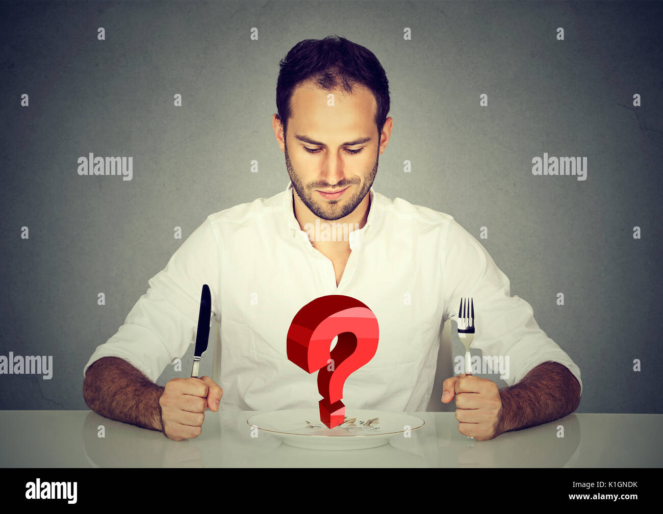 Man with fork and knife sitting at table looking at empty plate with big red question Stock Photo
