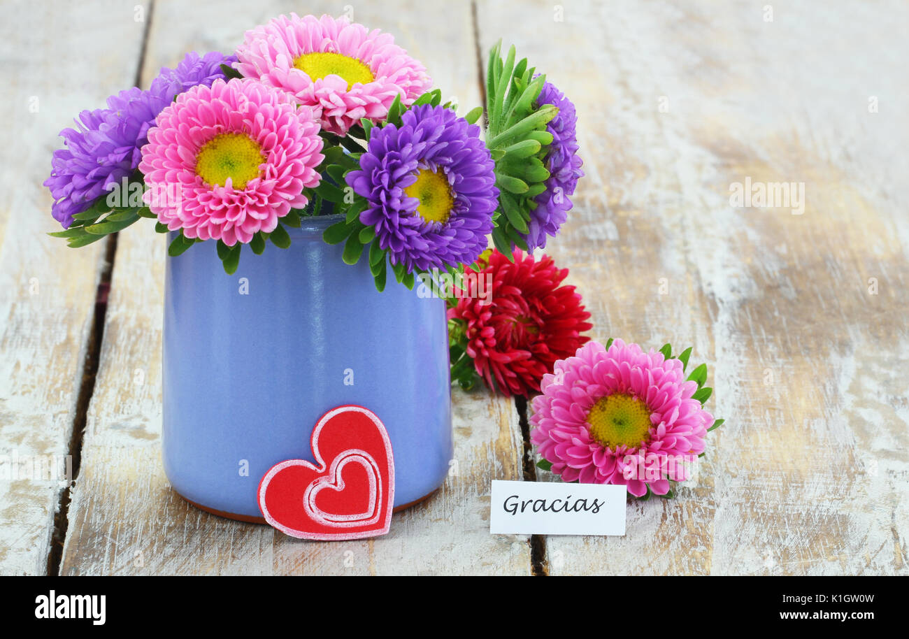 Gracias (thank you in Spanish) with colorful daisy flowers in blue vase on wooden surface Stock Photo