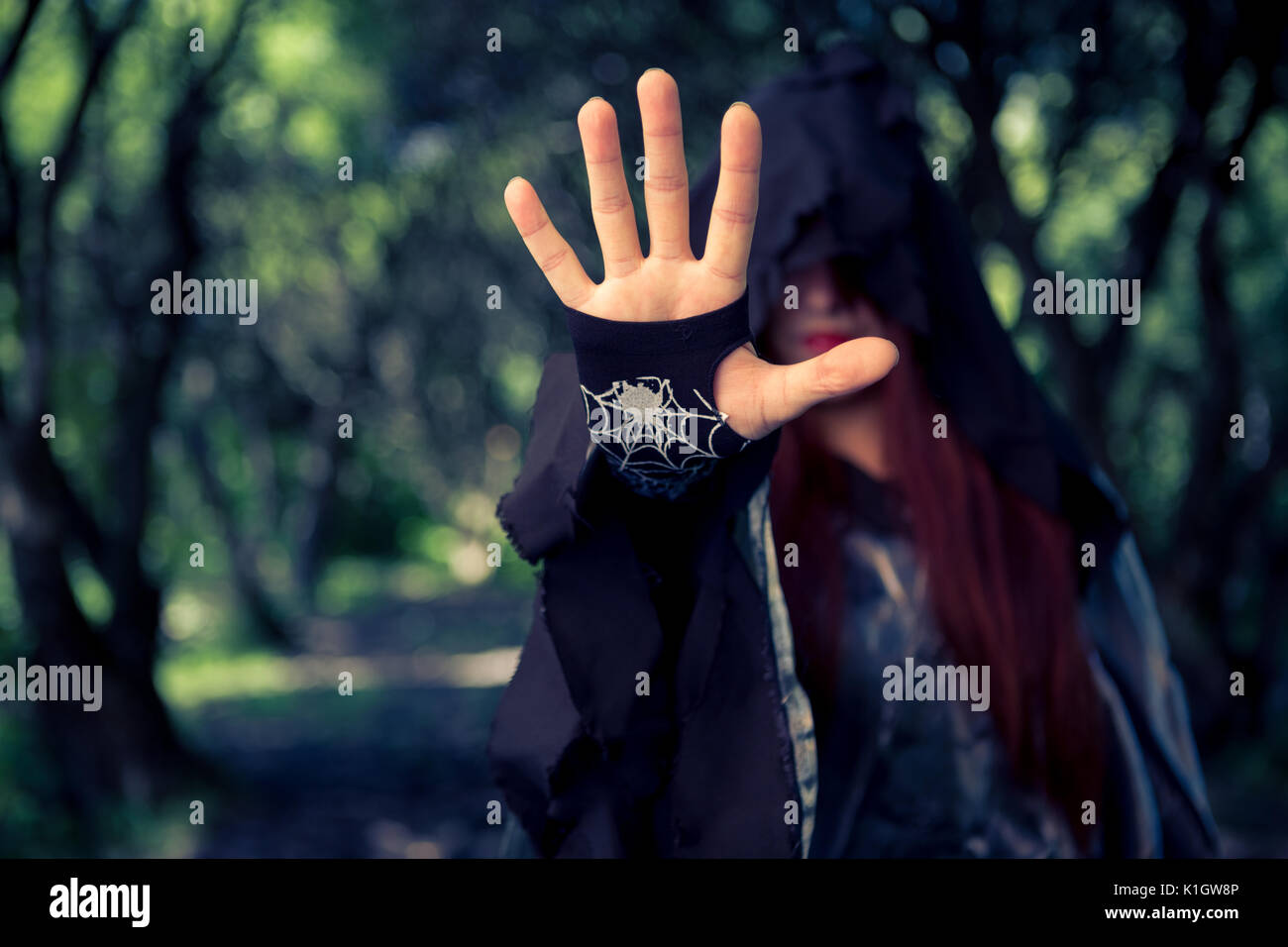 Picture of witch in hood with outstretched hand in forest Stock Photo