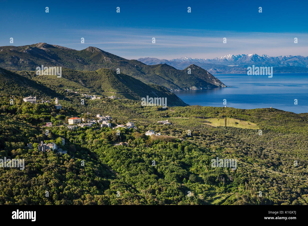 Mediterranean Sea coast, snowcapped peaks of Monte Cinto mountain range in far distance, village of Camera, in commune of Centuri, Cap Corse, Corsica Stock Photo