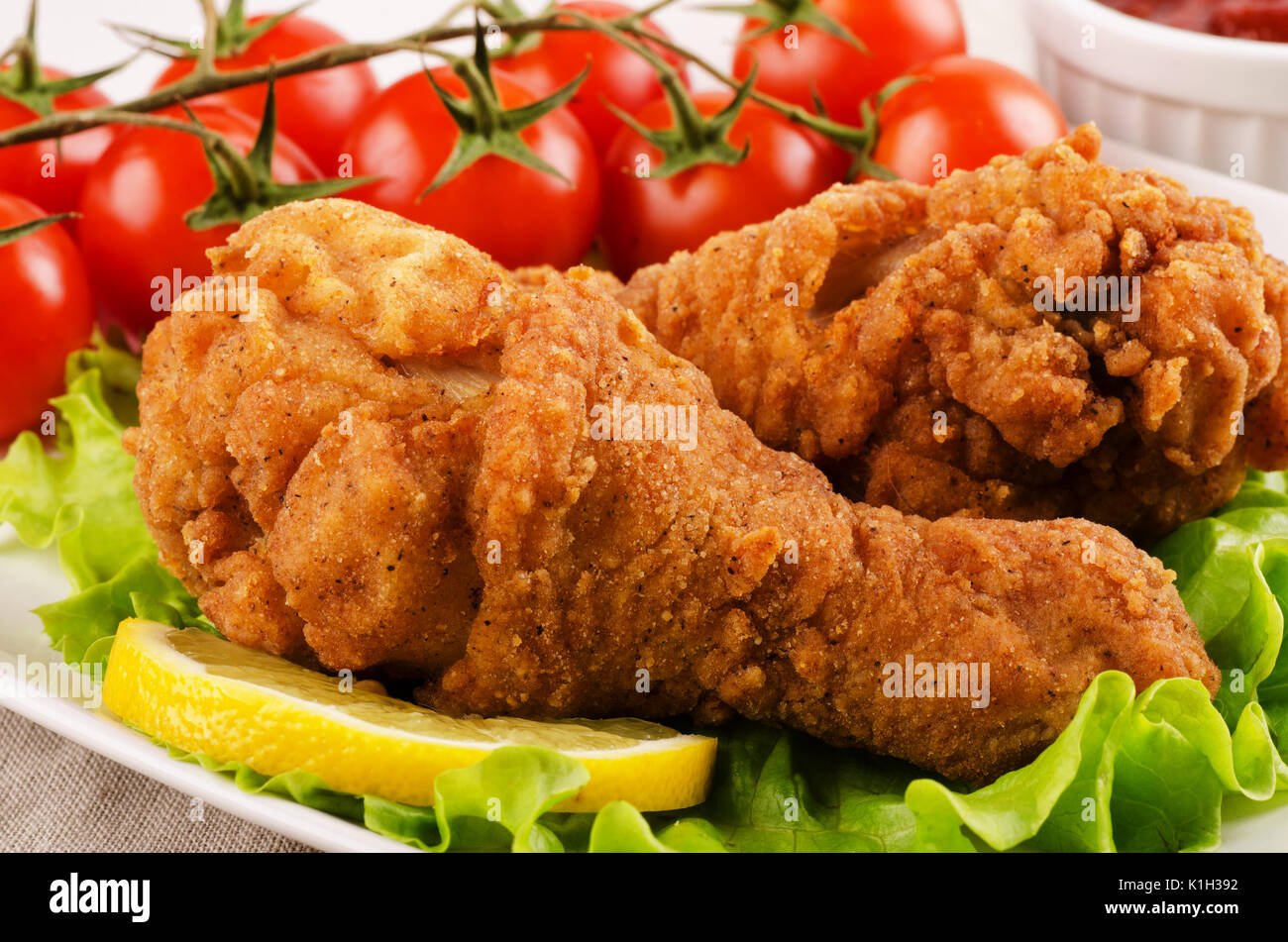 Chicken drumsticks in breadcrumbs with tomatoes and salad close-up Stock Photo
