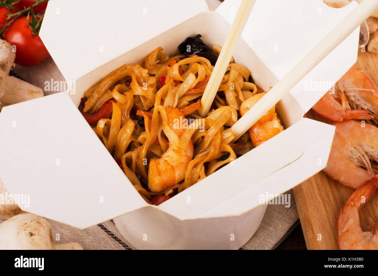 Noodles with vegetables, shrimp with chopsticks on a dark wooden background in a white box Stock Photo