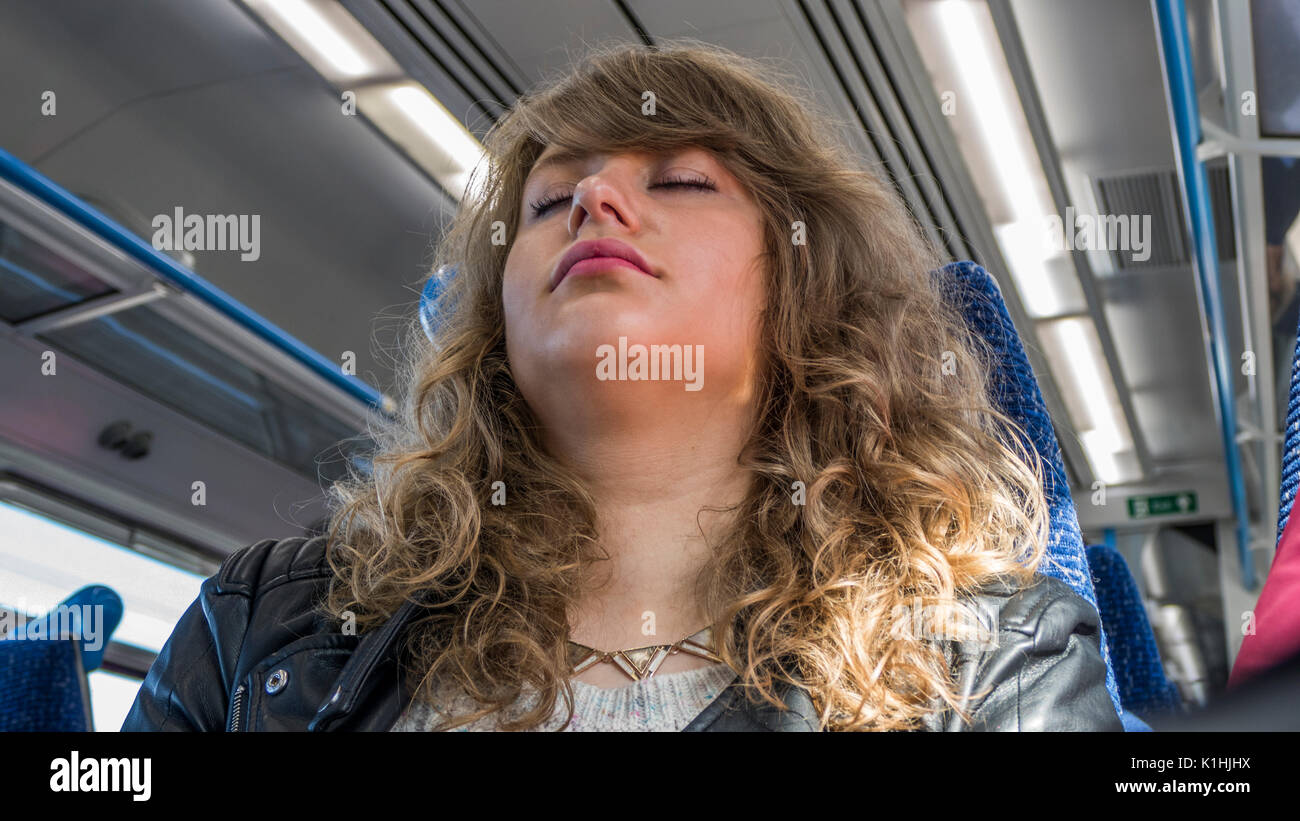 Pretty young woman with long curly hair, head back, eyes closed, asleep in her seat on a train journey to Paris. England. UK. Stock Photo