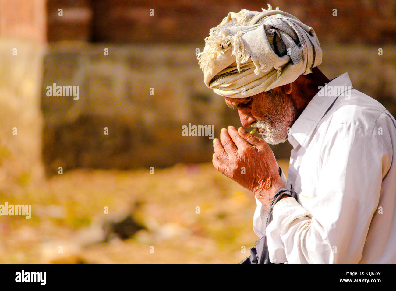 An Old Indian man is smoking beedi(an Indian cigar) in his leisure time. Stock Photo