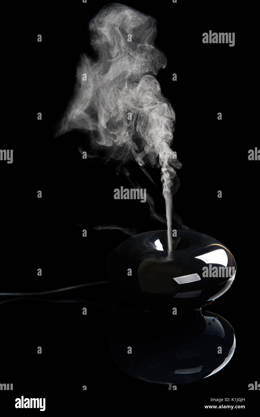 Black plastic aroma diffuser with streaming smoke on black reflecting