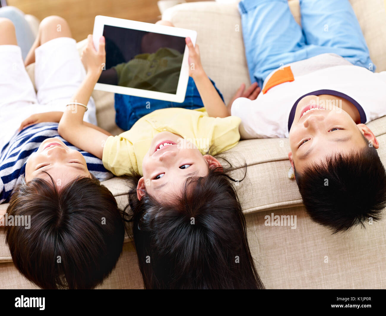 three asian children having fun lying upside down on couch. Stock Photo