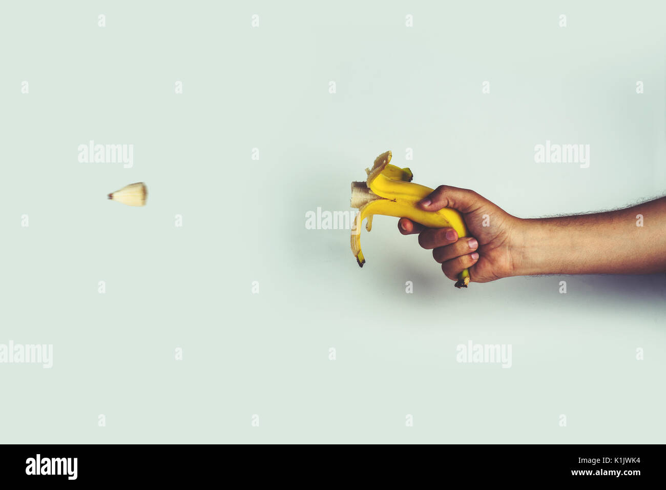 hand holding a banana like a gun and shooting a bite Stock Photo