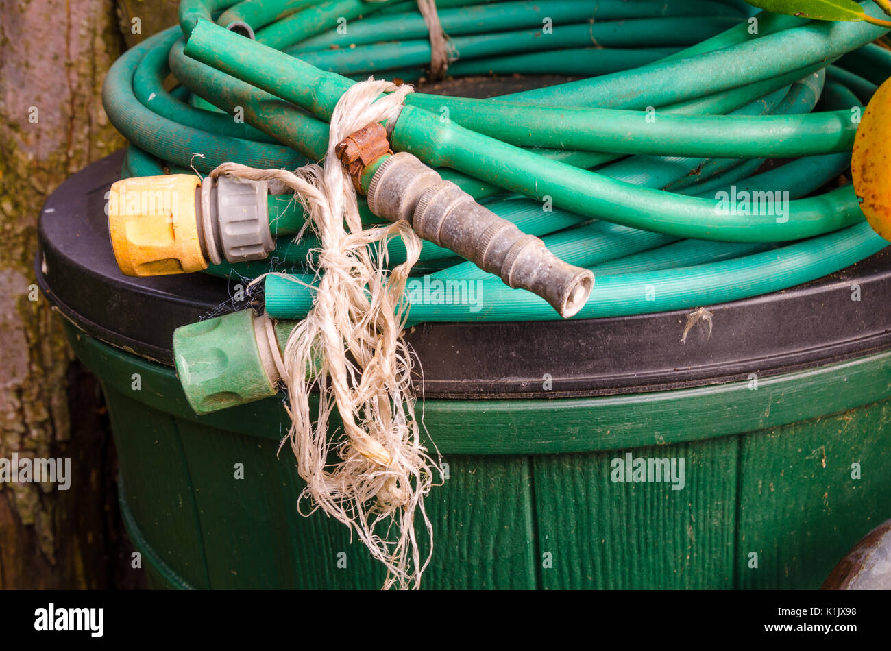 An old hose pipe with tap connectors and a spray nozzle curled up and left  on top of a bin in a back garden Stock Photo - Alamy