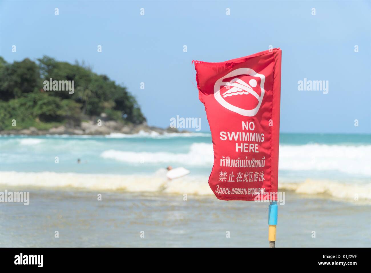 No swimming here sign dangerous area of the beach red flag in English and Thai text Stock Photo