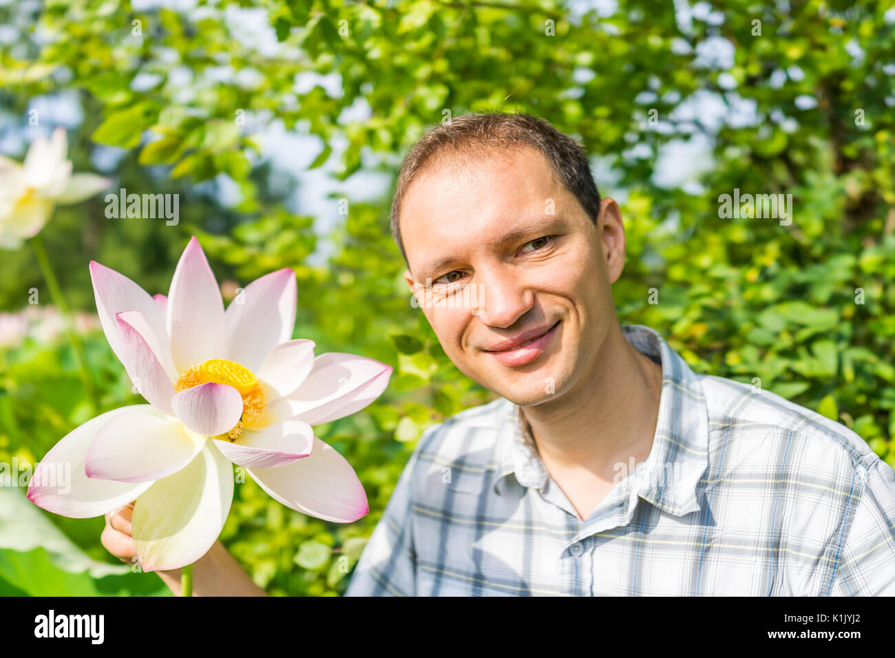 Portrait closeup of young man smiling holding bright white and pink lotus flower with yellow seedpod inside Stock Photo