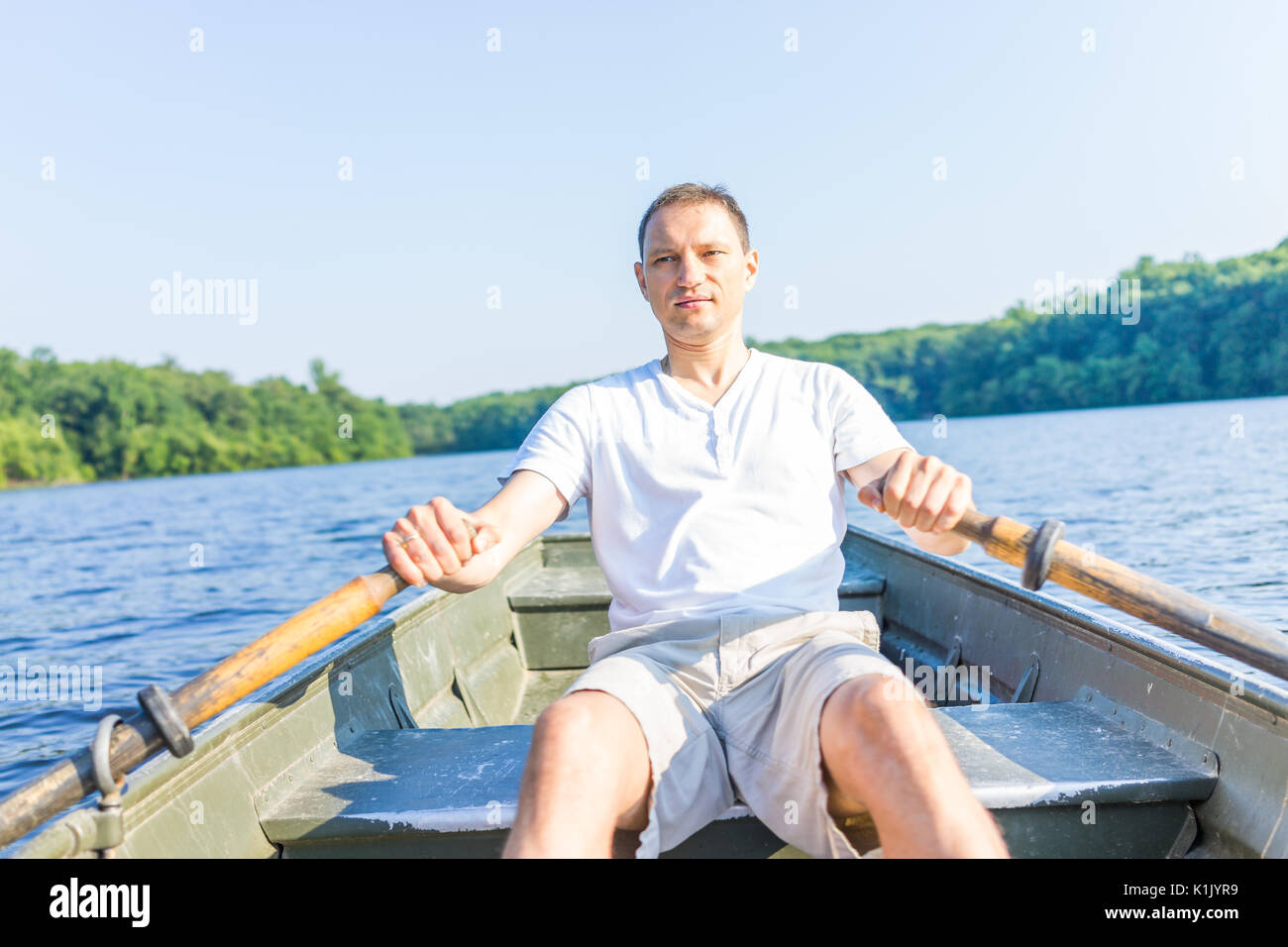 Serious young man rowing boat on lake in Virginia during summer in white shirt Stock Photo