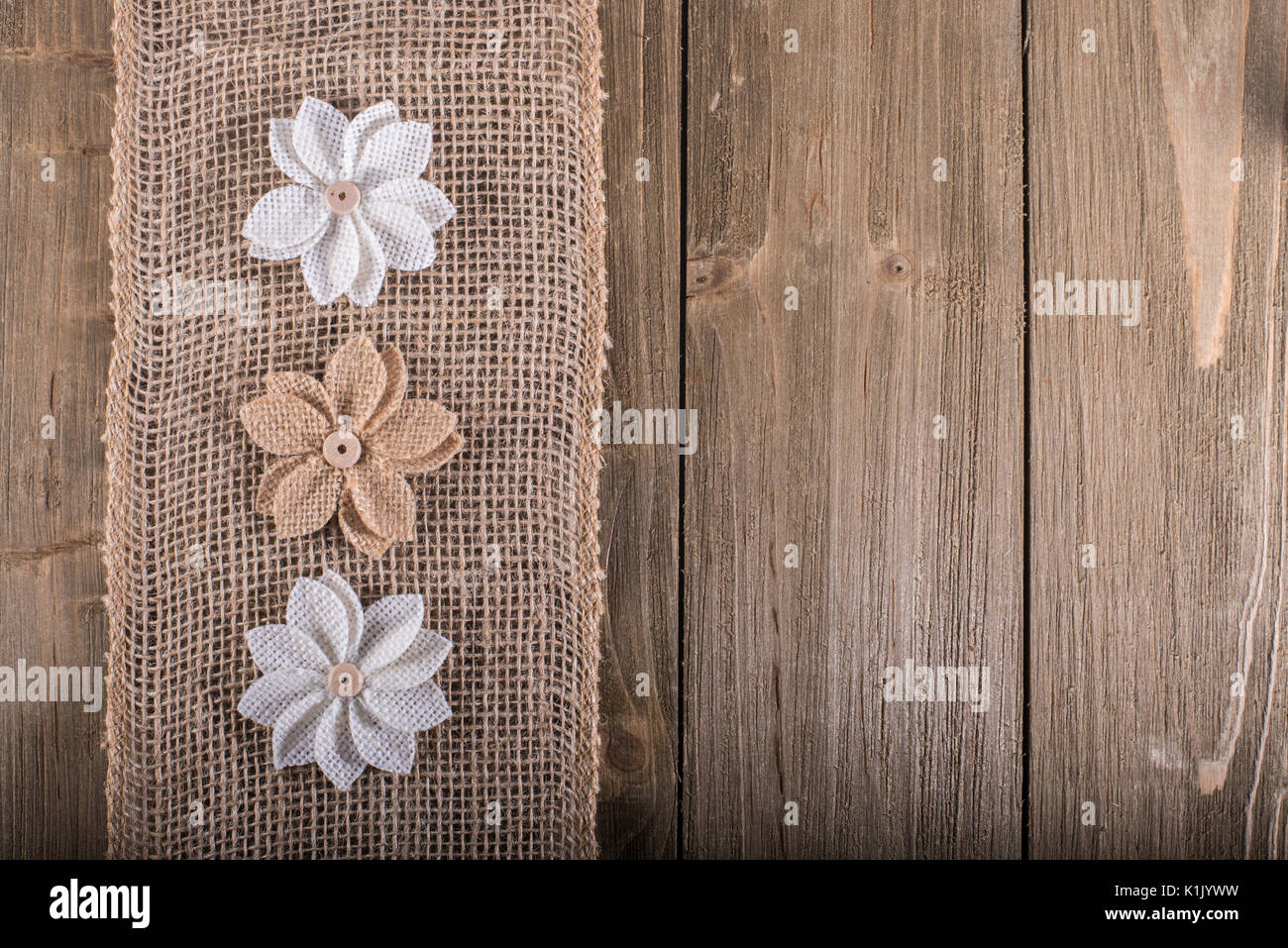 Three burlap flowers on burlap stripe on wood background with space