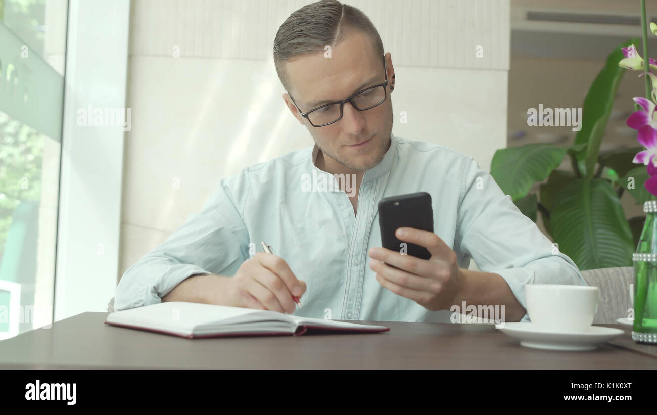 Businessman writing in daily planner and check notes on smartphone Stock Photo