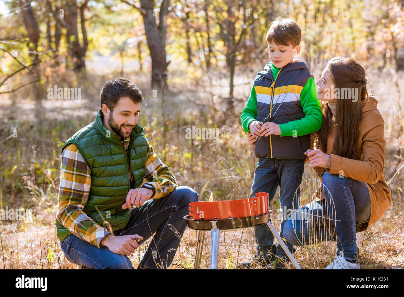 Portrait of happy family with one child preparing barbecue on grill in autumn park Stock Photo