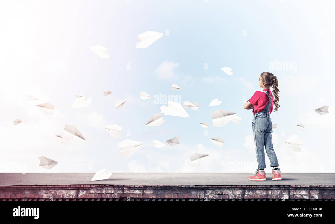 Cute kid girl standing on building roof and paper planes flying around ...