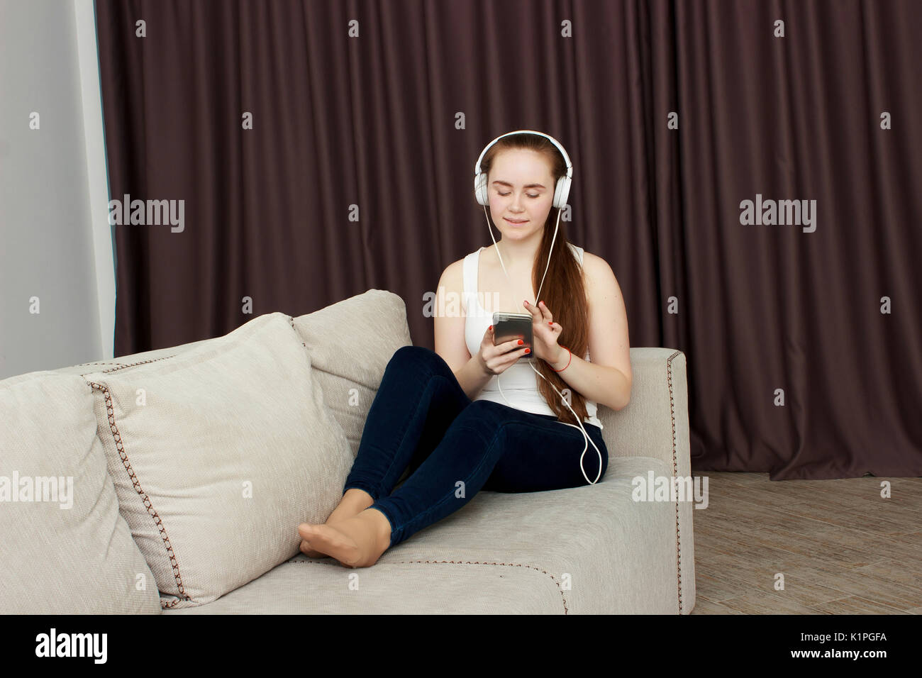 Woman listening music in headphones sitting on sofa in room Stock Photo