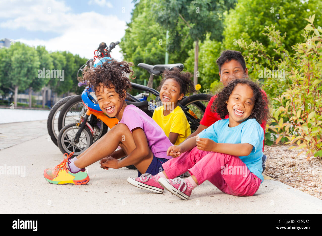 Group of African children sitting on the bike path after cycling in summer park Stock Photo