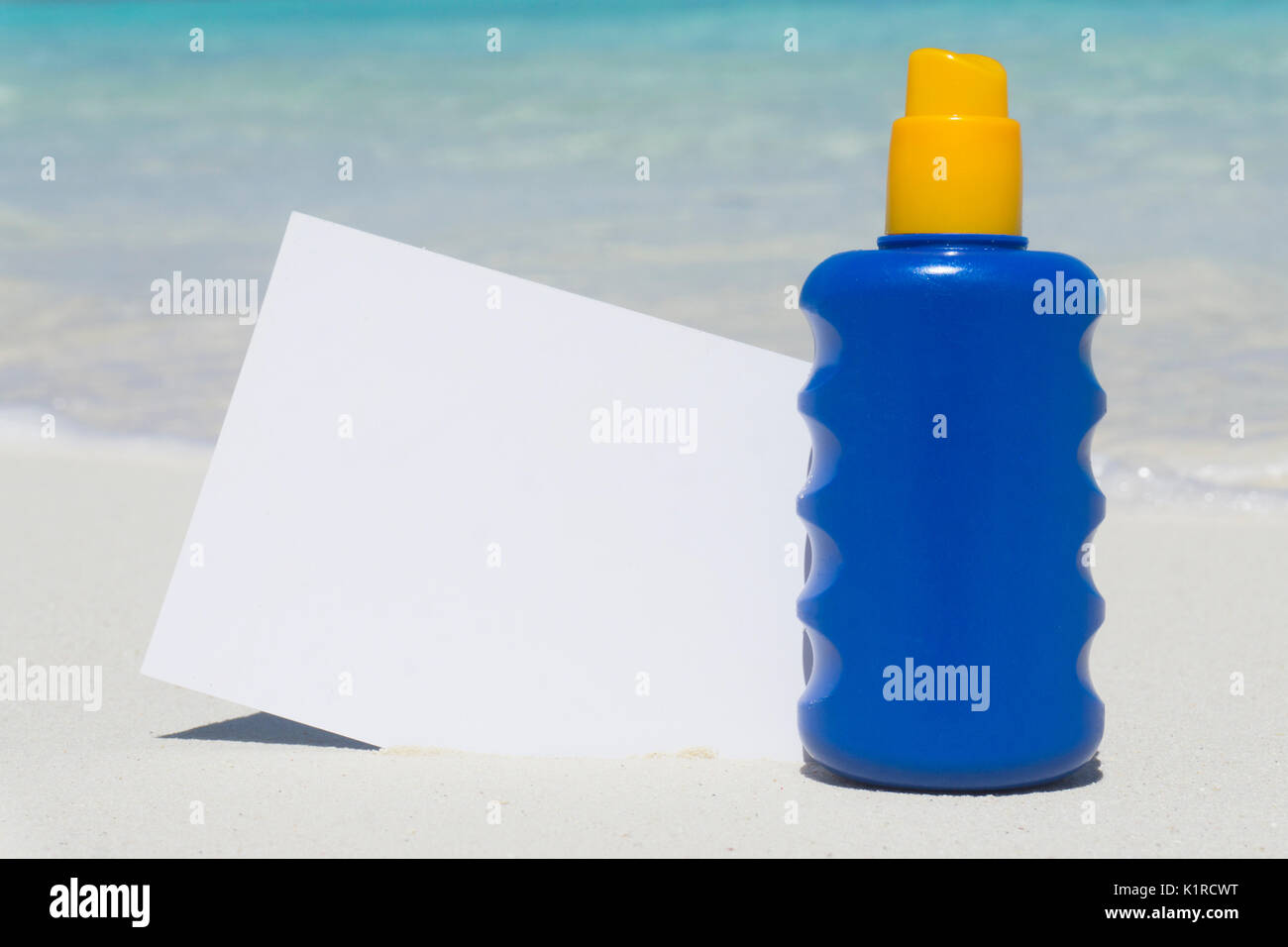 Bottle of sun lotion suncream protection and blank note on a tropical beach Stock Photo