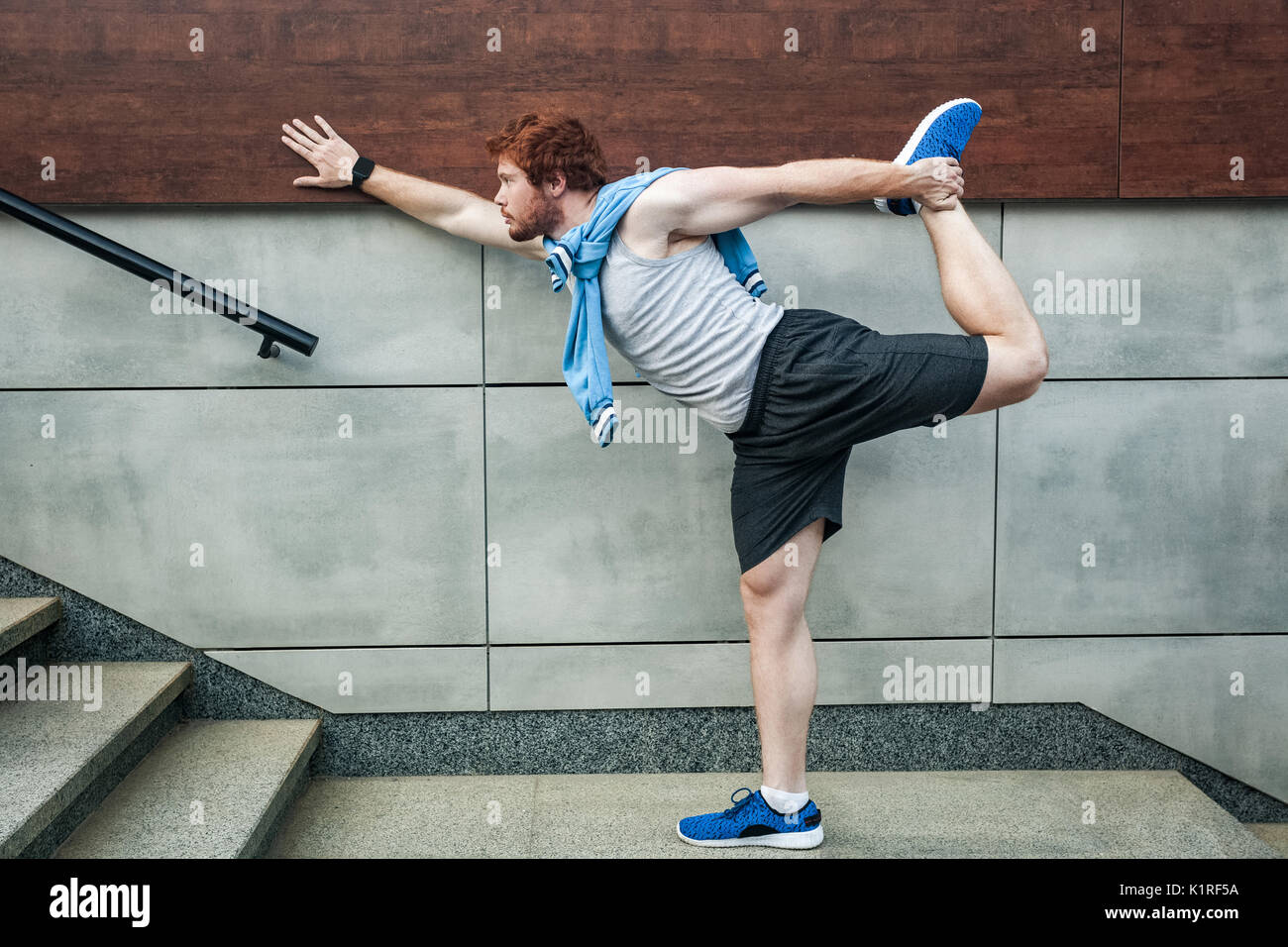 Fitness sport young adult redhead man in sportswear doing yoga fitness exercise in the city street over gray concrete background. Outdoor sports cloth Stock Photo