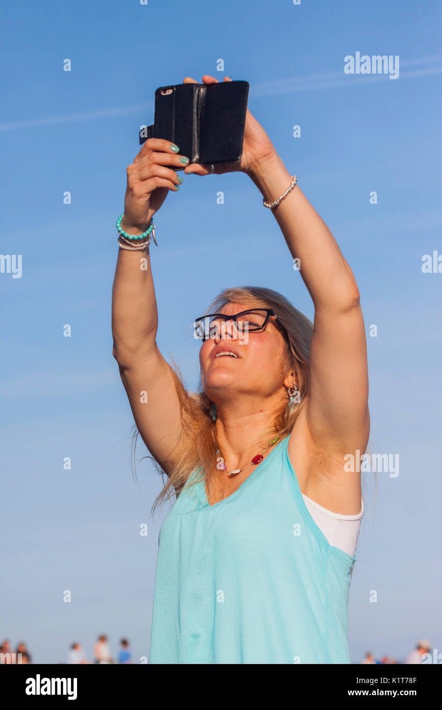 A young woman takes photos videos using a mobile phone on a beach. Stock Photo