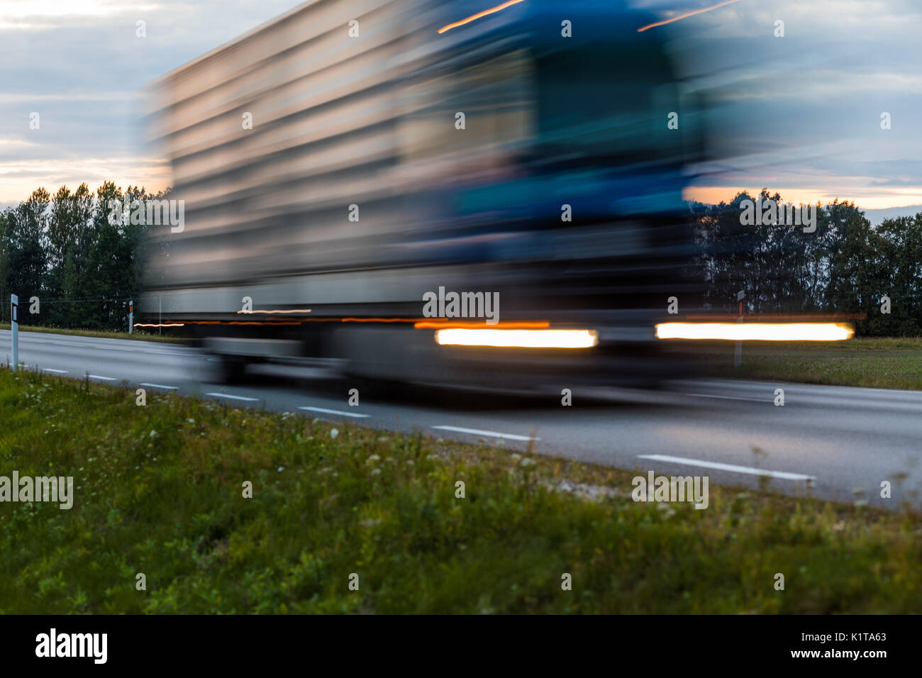 Speeding motion blur oncoming trucks with glowing lights on the highway after sunset. Abstract blur image background with copy space. Stock Photo