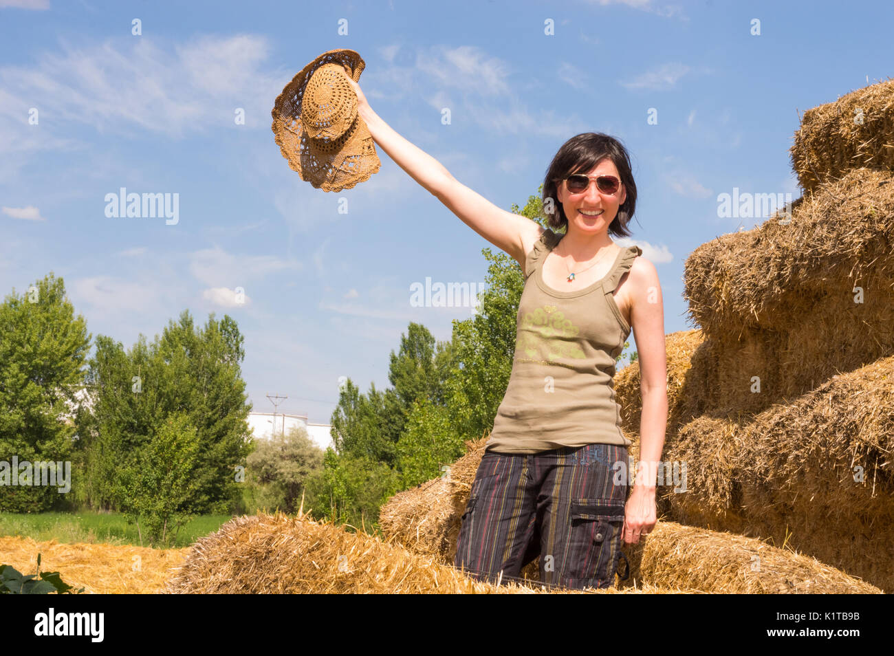 Pretty happy woman standing in a straw bale and holding her hat in her hand. Stock Photo