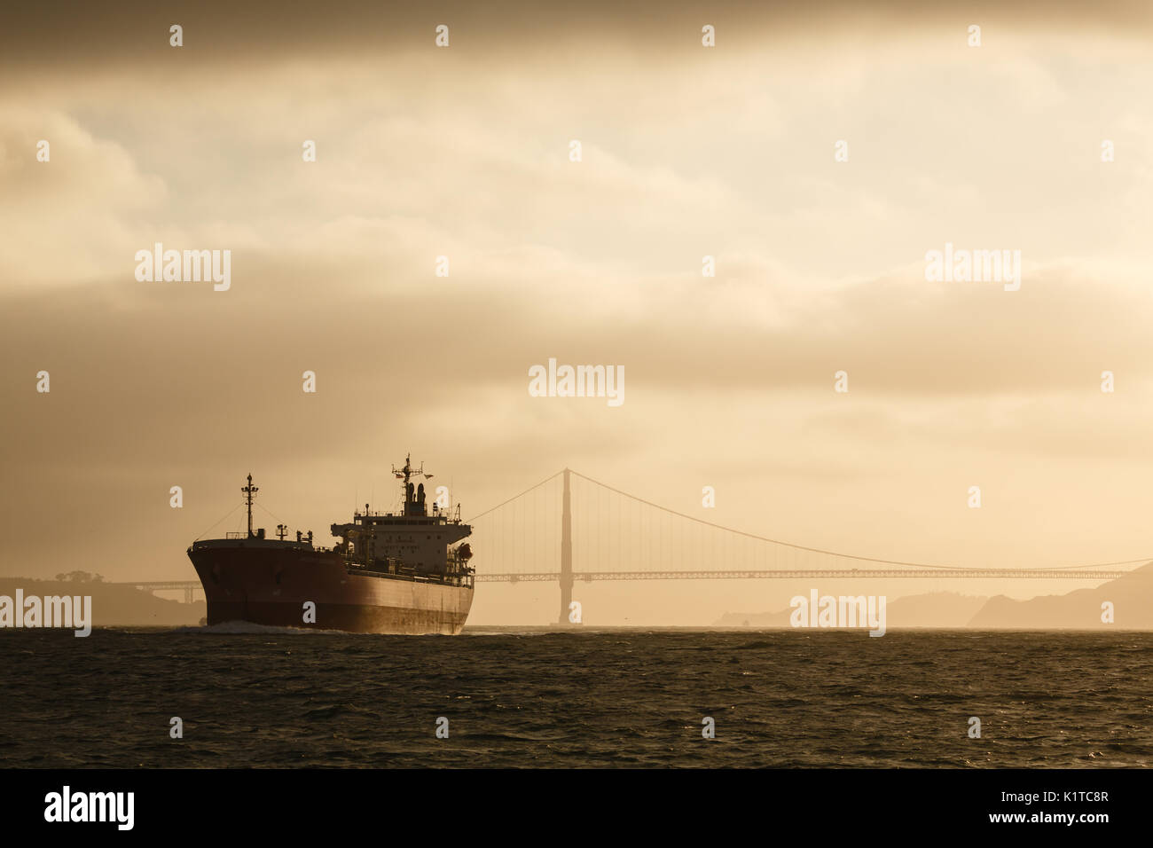 Giant tanker ship leaves golden gate bridge behind at sunset Stock Photo