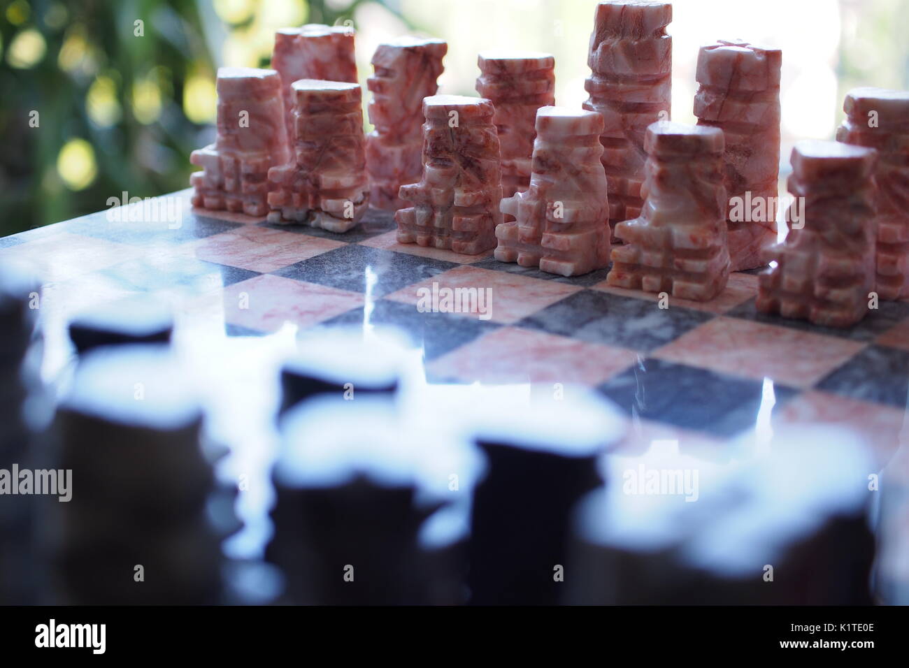 Marble chess pieces (pink and black) face each other across the chessboard. Stock Photo