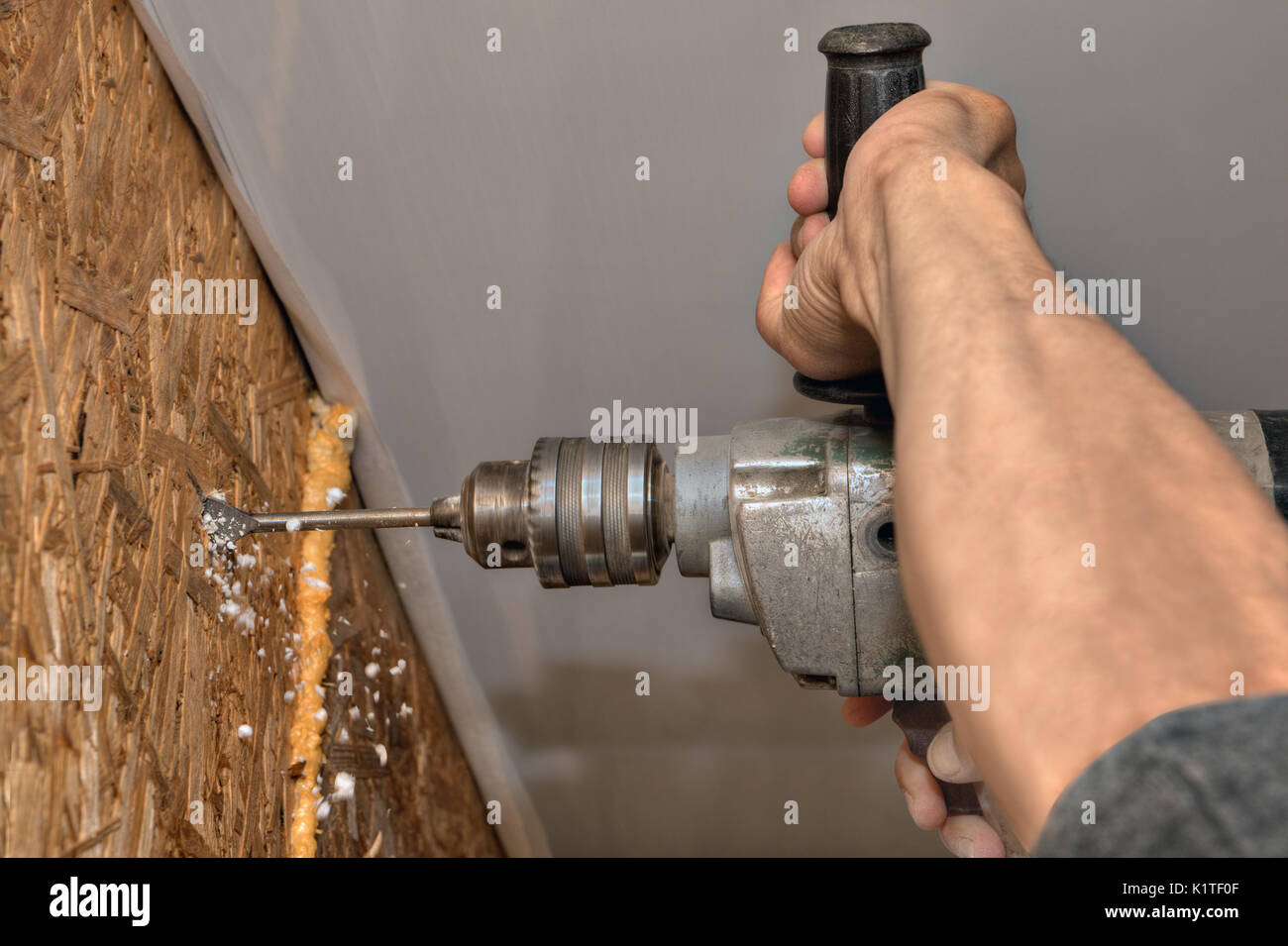 Builder drills in wooden wall communication hole, working hand close-up. Stock Photo