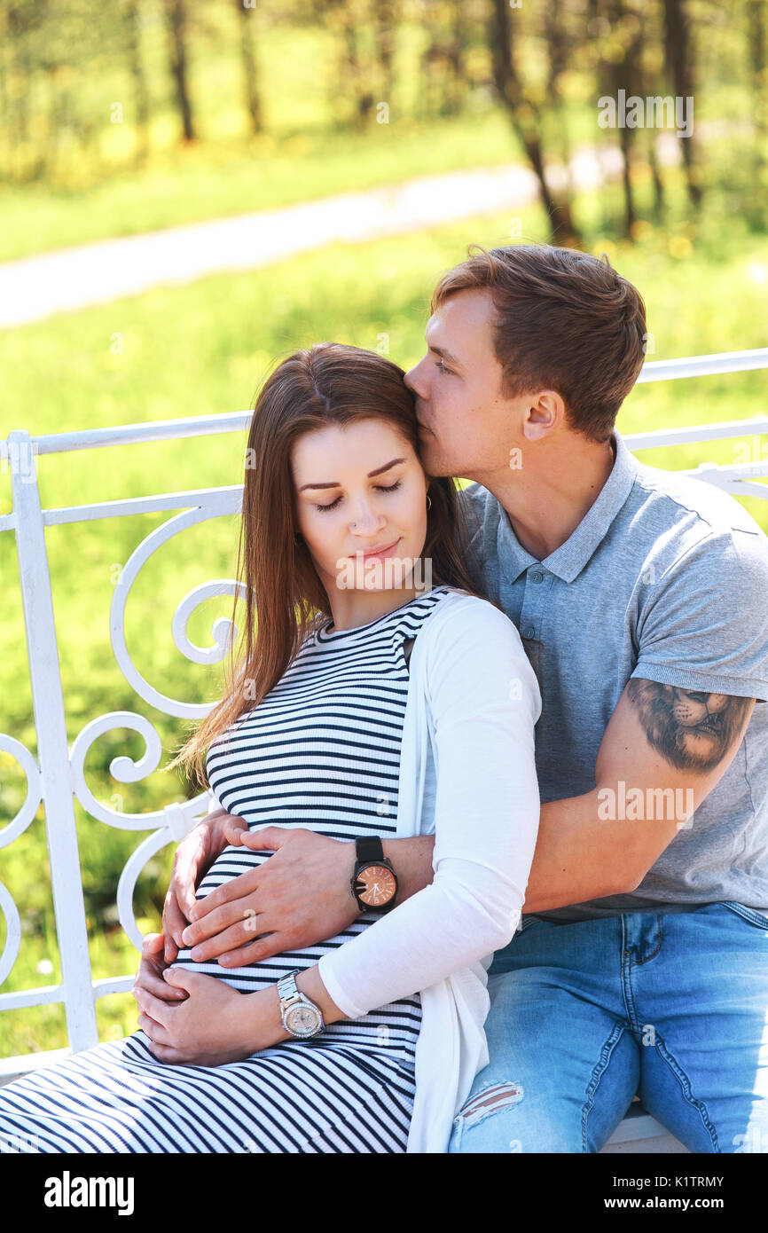 Handsome man and his beautiful pregnant wife are hugging and smiling ...