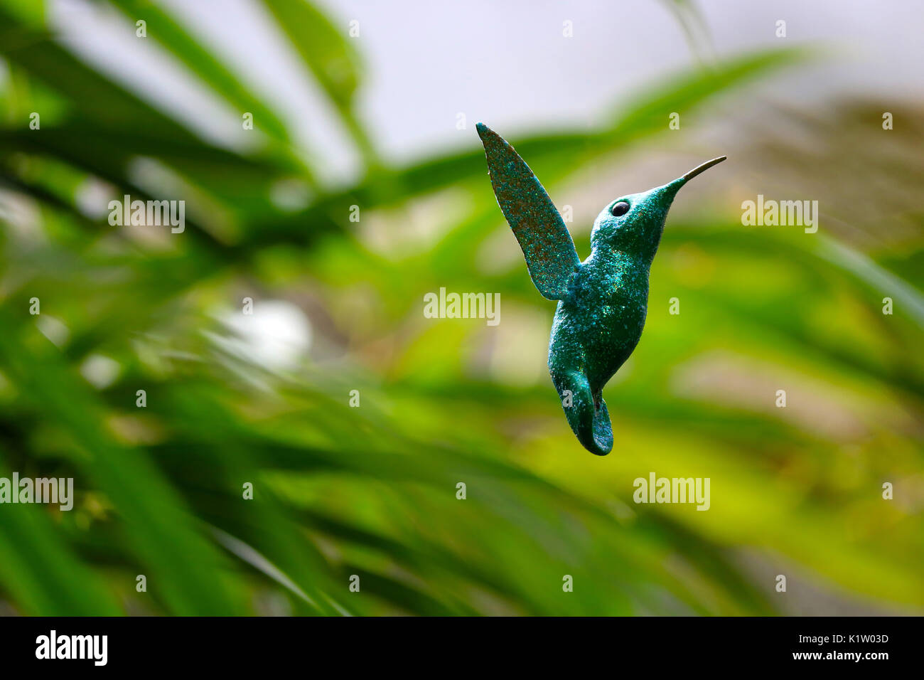 glittering green artificial fake hummingbird hovering in front of green leaves stems plants Stock Photo