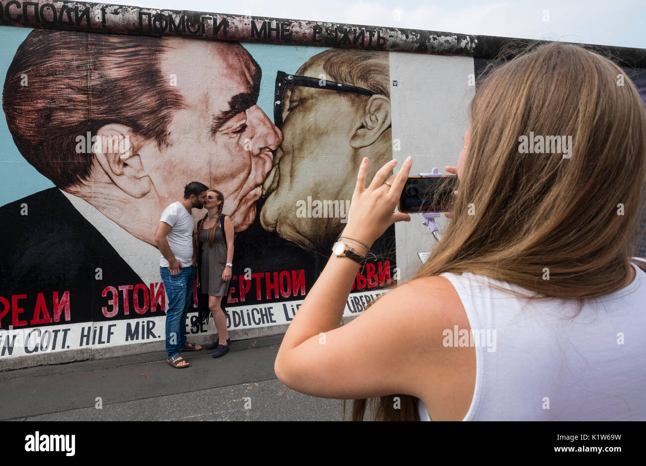 Tourist taking photograph of mural painted on original section of Berlin Wall at East Side gallery in Berlin, Germany Stock Photo