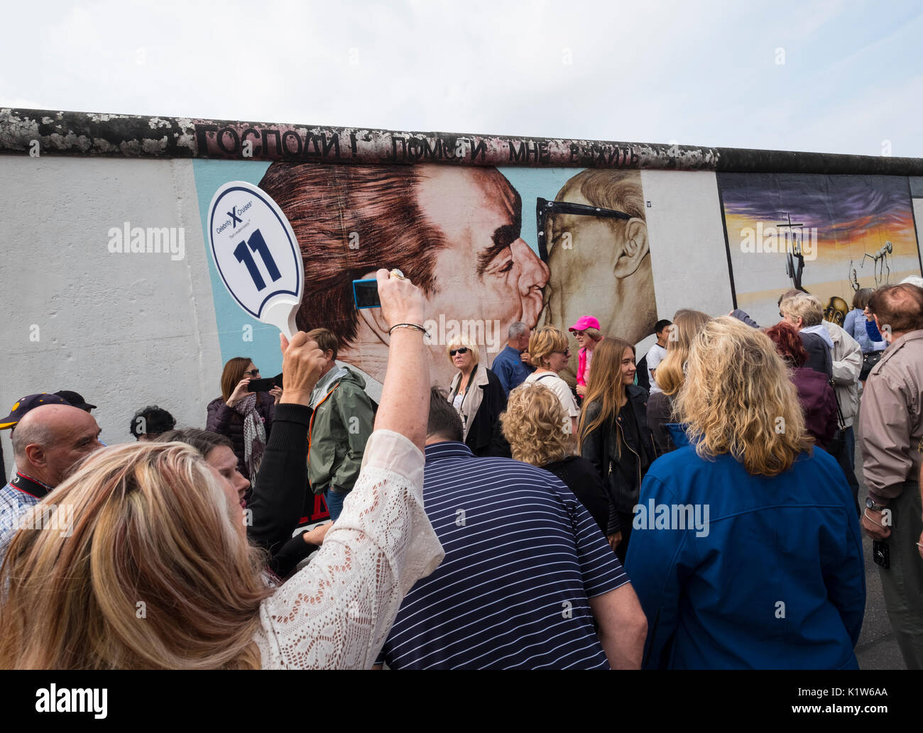 Large tour group taking photos of mural The Kiss painted on original section of Berlin Wall at East Side gallery in Berlin, Germany Stock Photo