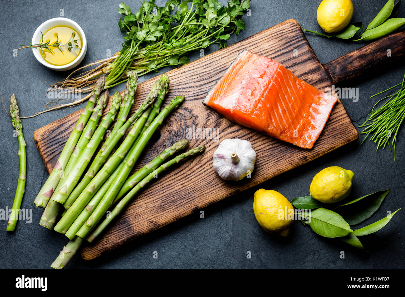 Ingredients for cooking. Raw salmon fillet, asparagus and herbs on wooden board. Food cooking background with copy space. Top view Stock Photo