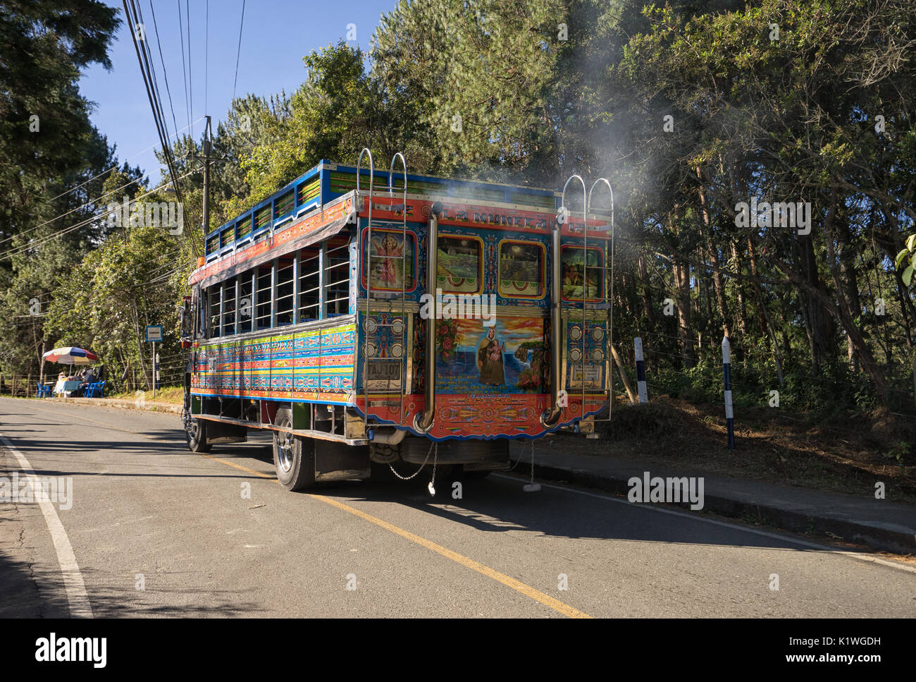 August 6, 2017 Medellin, Colombia: a colourful od bus called 'chiva' emiting high level of polution driving through a closeby park Stock Photo