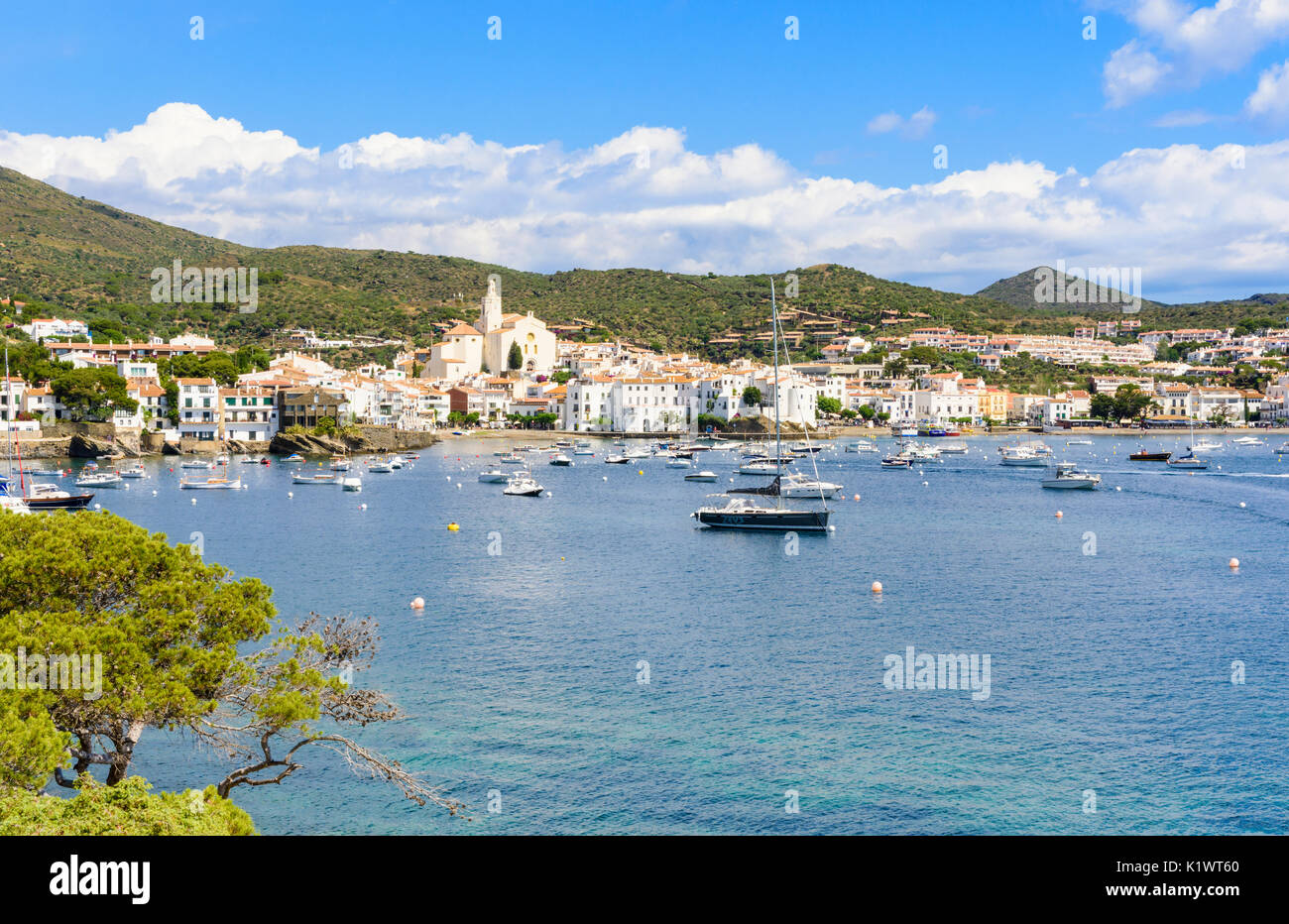Whitewashed Cadaqués Town, topped by the Church of Santa Maria overlooking boats in the blue waters of Cadaqués Bay, Catalonia, Spain Stock Photo