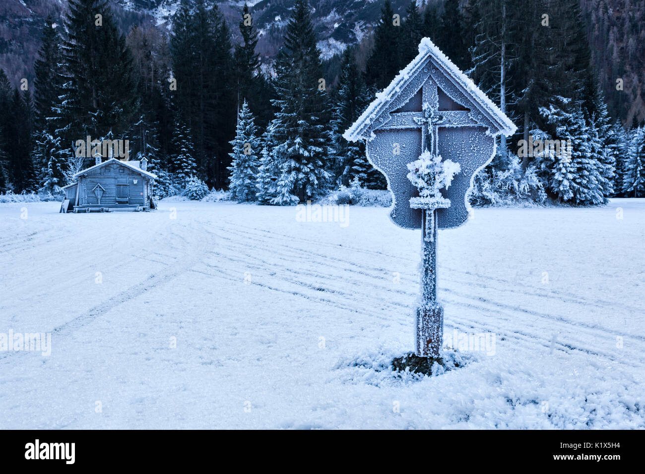 Europe, Italy, Veneto, Belluno. A wooden hut and a crucifix covered with ice in Ansiei valley in winter, Auronzo di Cadore, Dolomites Stock Photo