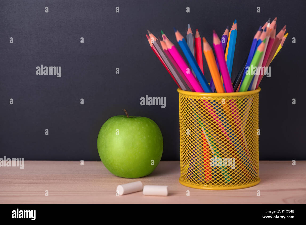 education concept with green apple, pencils, chalks over black chalkboard background, close up Stock Photo