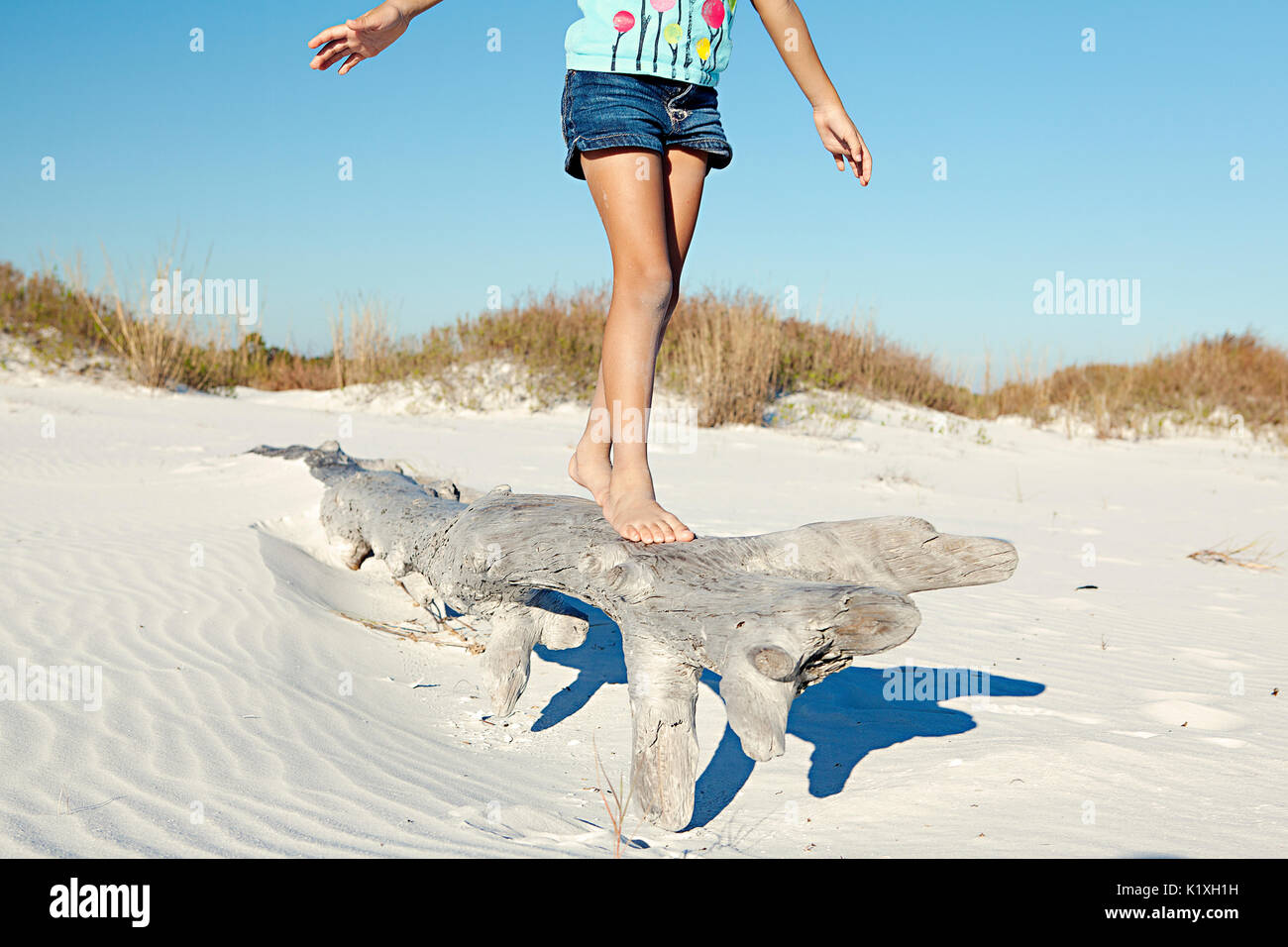 Young girl balancing on drift wood at the beach. Stock Photo
