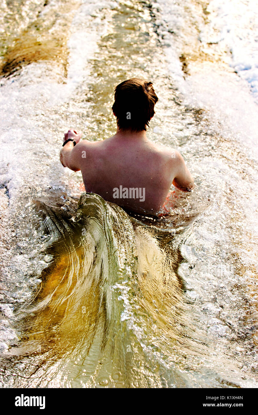Young man sliding on a dam overflow water slide. Stock Photo