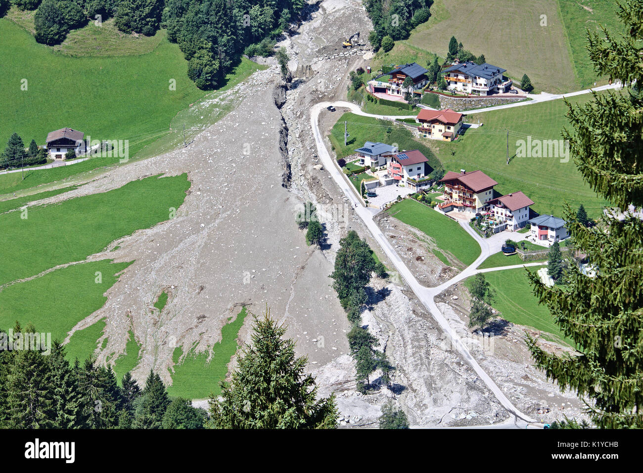 Aerial view of mountain stream in the Austrian Alps blocked after a massive mudflow with excavator and truck working to clean up and small village nea Stock Photo