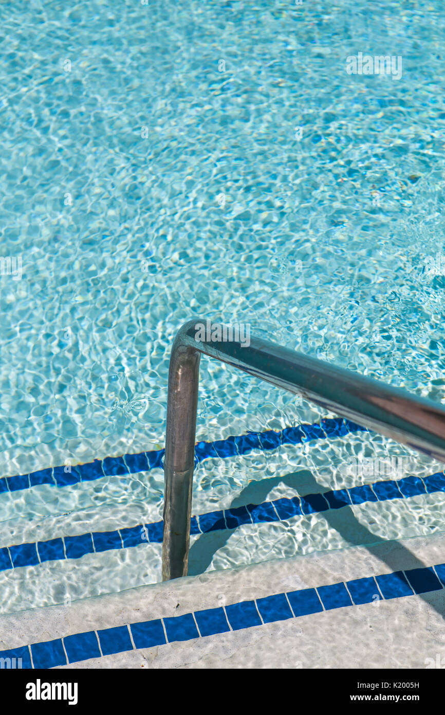 Sunlight glistening off the crystal clear water of a beautiful swimming pool.A view of pool steps enticing the viewer into the cool water on a hot day Stock Photo