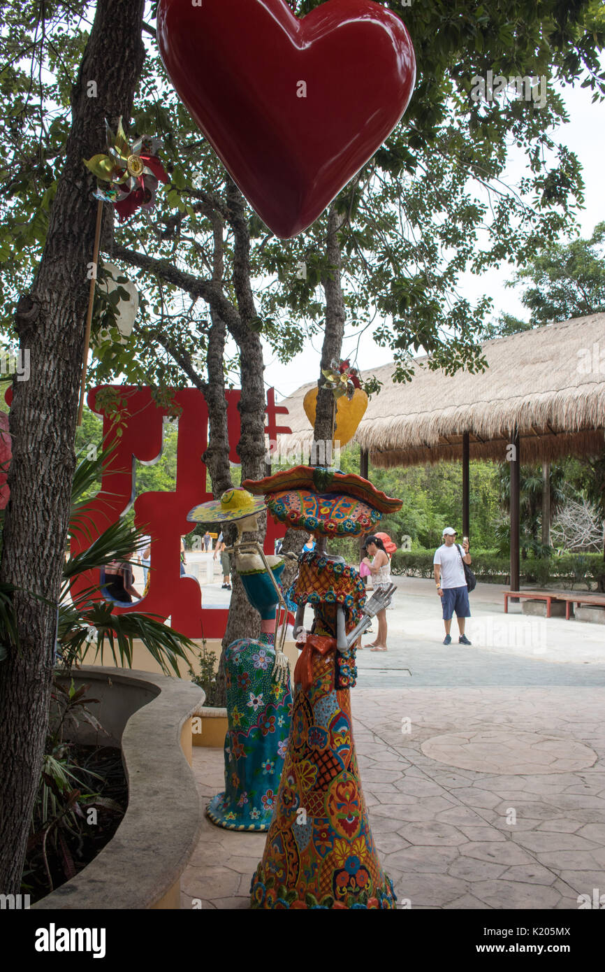 Large red and smaller yellow hearts hanging in trees with Mexican Calaca in bright colored dresses. Stock Photo