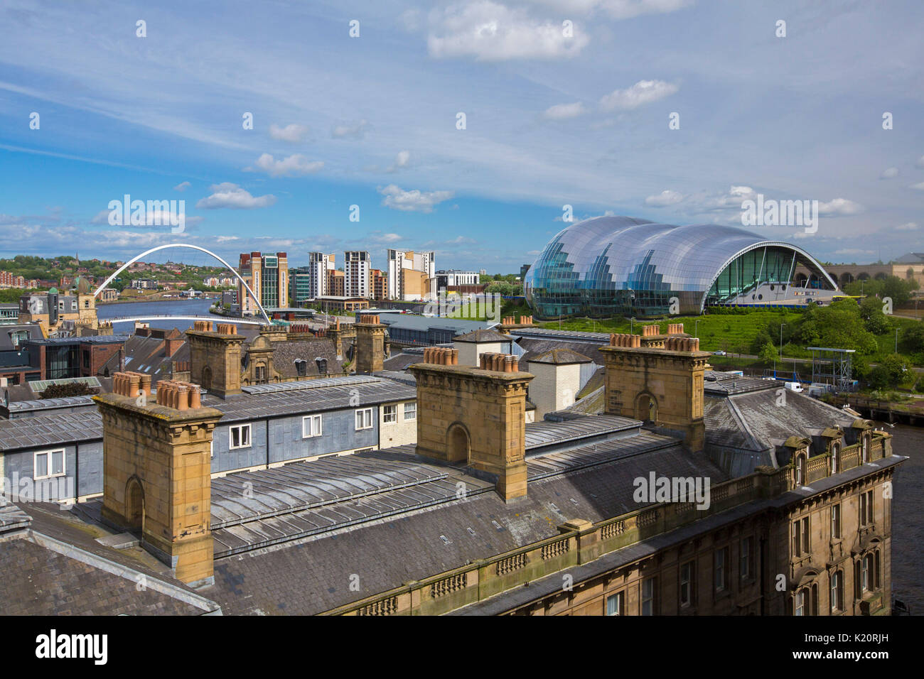 View across city rooftops of Gateshead Sage, a modern glass building, &  millennium bridge crossing Tyne river under blue sky at Newcastle-upon-Tyne Stock Photo