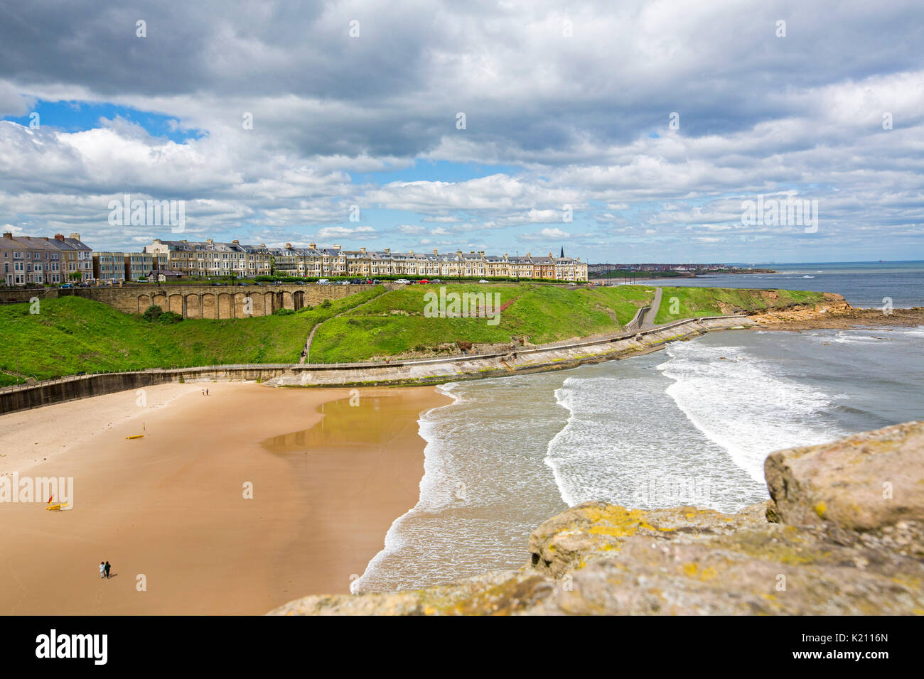 Buildings and guesthouses at Tynemouth on clifftop towering above sandy beach and ocean under blue sky, viewed from ruins of historic  castle, England Stock Photo