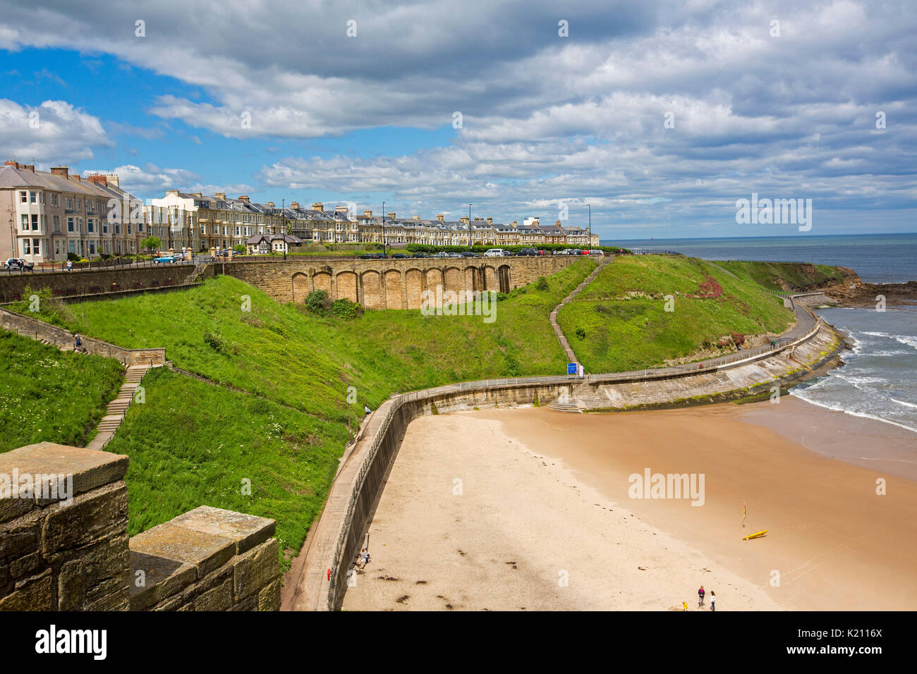 Buildings and guesthouses at Tynemouth on clifftop towering above sandy beach and ocean under blue sky, viewed from ruins of historic  castle, England Stock Photo